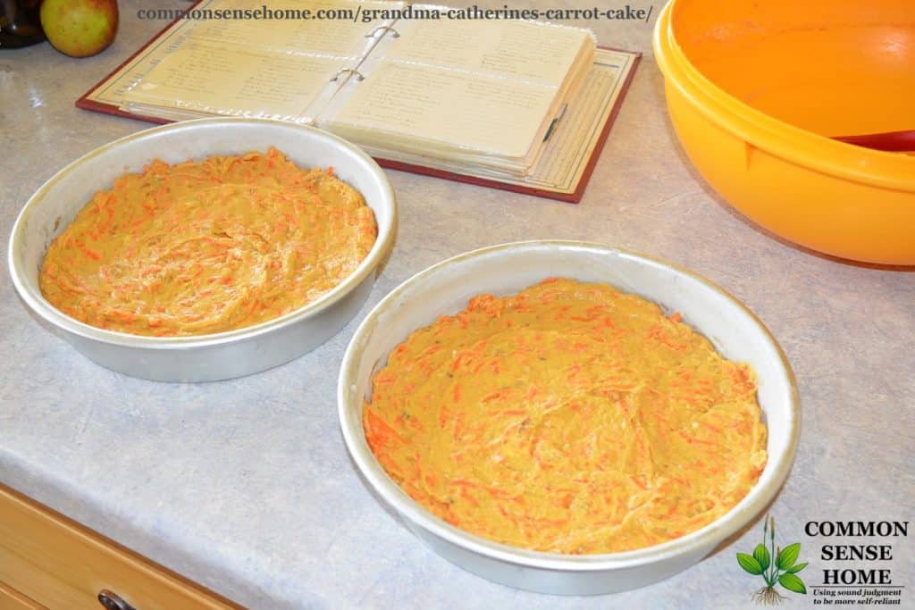 carrot cake batter in round pans with cookbook and yellow bowl