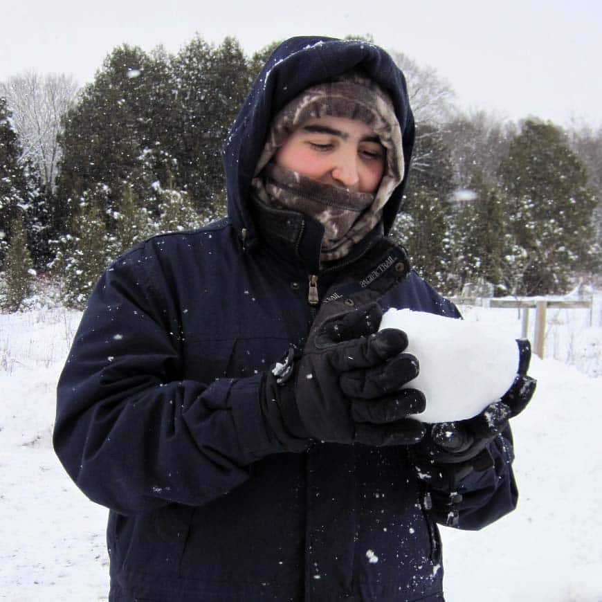 young man holding snowball wearing winter clothes