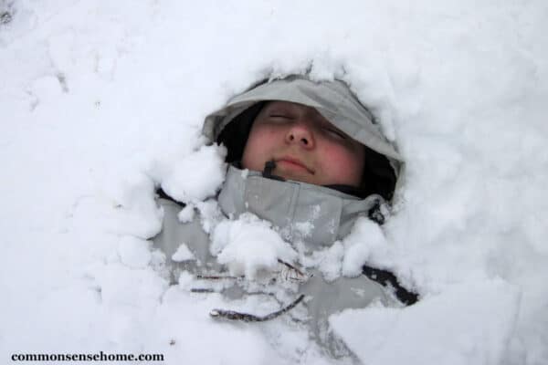 boy wearing cold weather clothing buried in snow with face showing