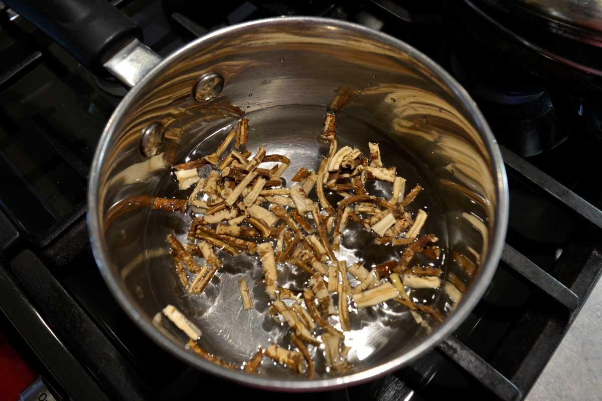 dandelion root decoction with root pieces cooking in small pot