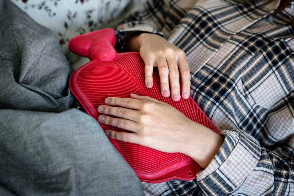 woman uses hot water bottle on midsection to provide comfort for UTI